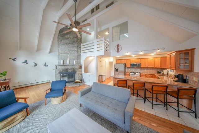 living room featuring baseboard heating, high vaulted ceiling, beam ceiling, ceiling fan, and a stone fireplace