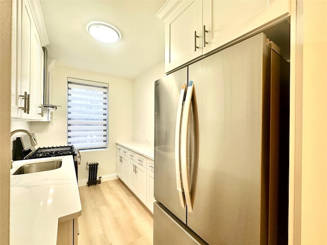 kitchen with white cabinetry, stainless steel refrigerator, light stone counters, and sink