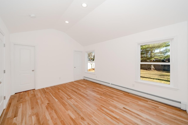 empty room featuring a baseboard heating unit, light wood-type flooring, vaulted ceiling, and a healthy amount of sunlight