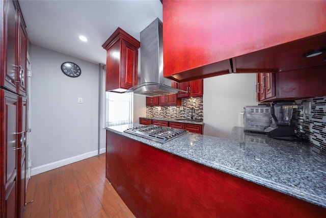 kitchen featuring decorative backsplash, dark stone counters, island range hood, stainless steel gas cooktop, and dark hardwood / wood-style floors