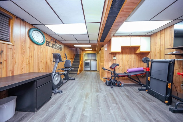 workout area featuring a paneled ceiling, light hardwood / wood-style floors, washer / clothes dryer, and wood walls