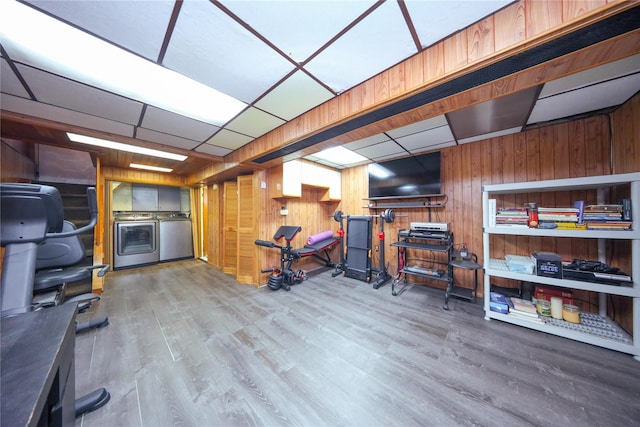 workout room featuring a drop ceiling, independent washer and dryer, wood-type flooring, and wooden walls