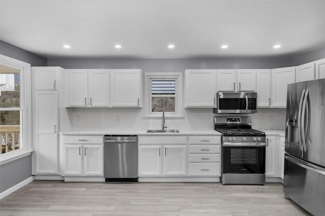 kitchen featuring appliances with stainless steel finishes, sink, white cabinets, light hardwood / wood-style flooring, and tasteful backsplash