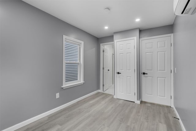 unfurnished bedroom featuring light wood-type flooring and a wall unit AC