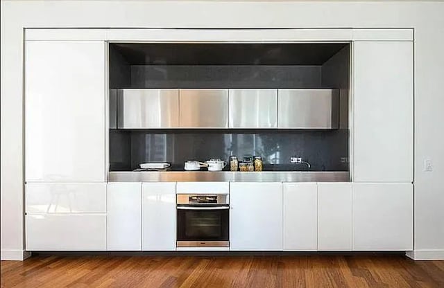 bar with dark hardwood / wood-style floors, stainless steel oven, and white cabinetry