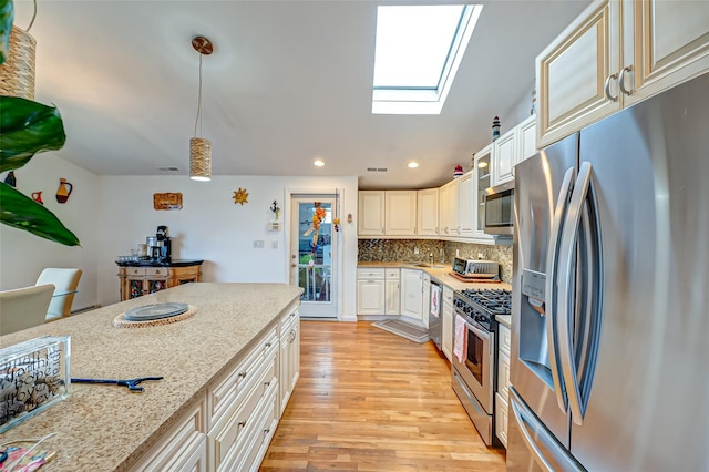 kitchen featuring light stone countertops, pendant lighting, appliances with stainless steel finishes, a skylight, and backsplash