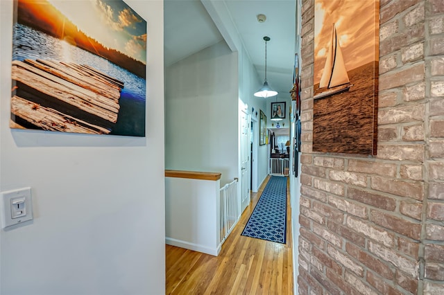 corridor featuring lofted ceiling, brick wall, and light hardwood / wood-style floors