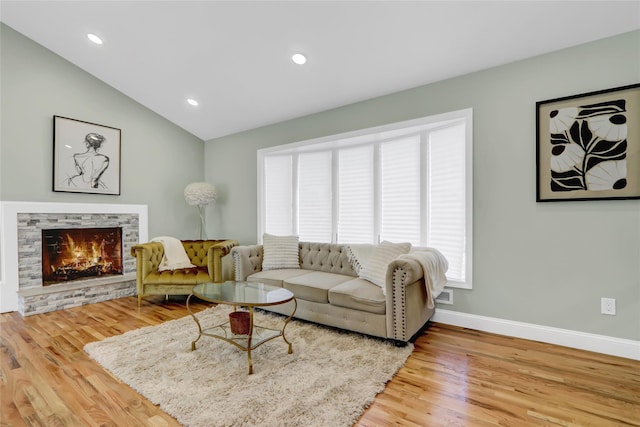 living room featuring vaulted ceiling, a stone fireplace, and hardwood / wood-style flooring