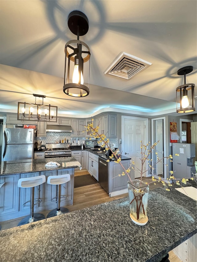 kitchen featuring extractor fan, hanging light fixtures, stainless steel appliances, gray cabinets, and backsplash