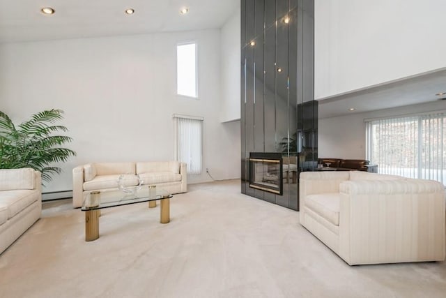 carpeted living room featuring a high ceiling, baseboard heating, and a fireplace