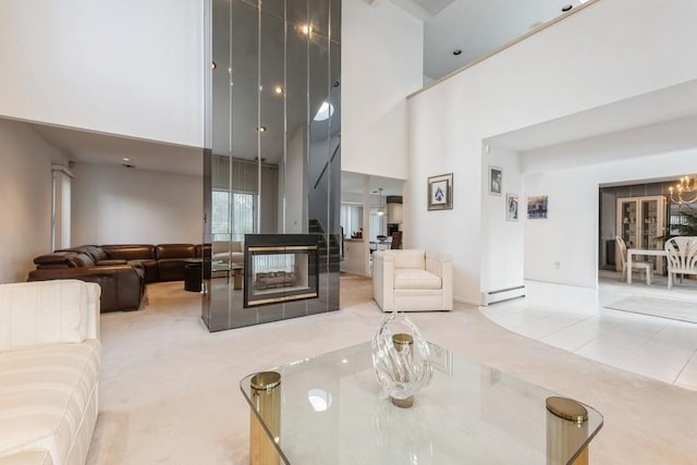 tiled living room with a towering ceiling, a multi sided fireplace, a baseboard heating unit, and an inviting chandelier