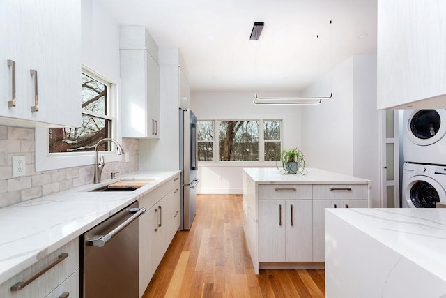 kitchen featuring appliances with stainless steel finishes, white cabinetry, sink, stacked washer and dryer, and light stone countertops