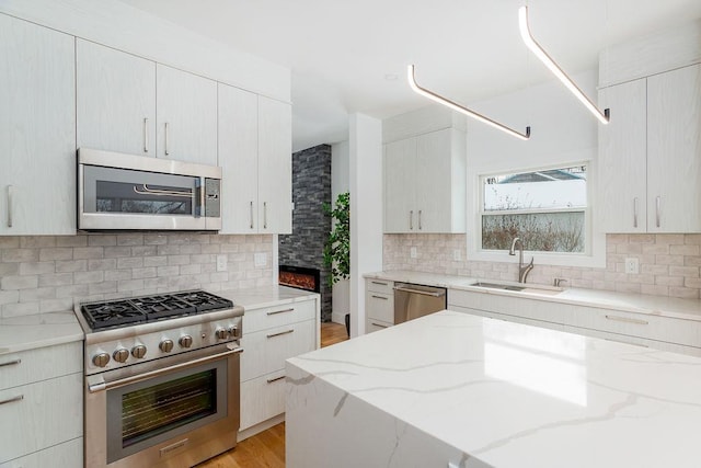 kitchen with sink, backsplash, stainless steel appliances, light stone countertops, and light hardwood / wood-style flooring