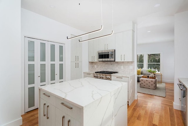 kitchen with white cabinetry, stainless steel appliances, a center island, light stone countertops, and decorative backsplash