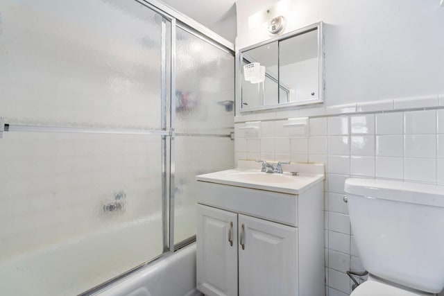 full bathroom featuring vanity, bath / shower combo with glass door, tile walls, and toilet