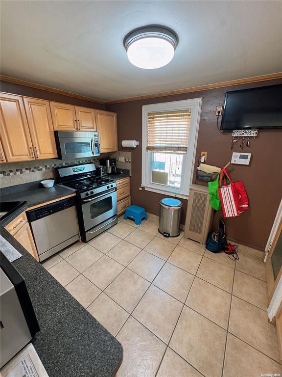 kitchen with tasteful backsplash, stainless steel appliances, crown molding, light tile patterned floors, and light brown cabinets