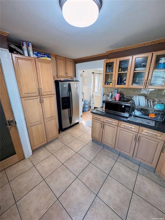 kitchen featuring decorative backsplash, light tile patterned floors, dark stone counters, and appliances with stainless steel finishes