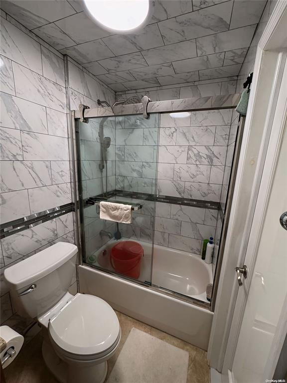 bathroom featuring toilet, tile walls, and combined bath / shower with glass door