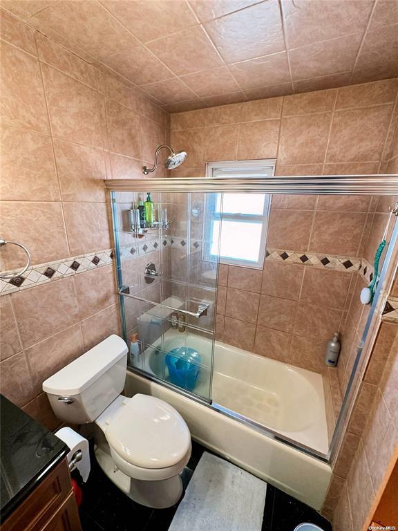 bathroom with toilet, enclosed tub / shower combo, and tile walls