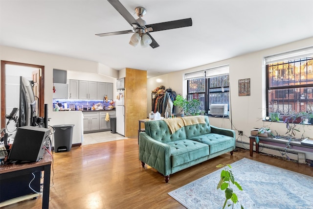 living room with light wood-type flooring, cooling unit, ceiling fan, and a baseboard heating unit