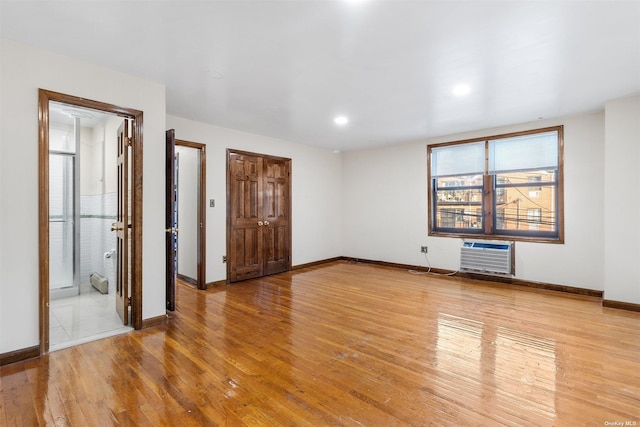 unfurnished bedroom with a wall mounted air conditioner, light hardwood / wood-style flooring, and ensuite bath