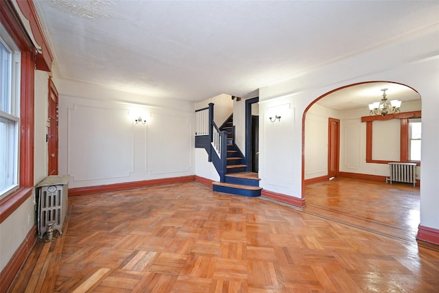 spare room with a chandelier, radiator heating unit, and light parquet floors