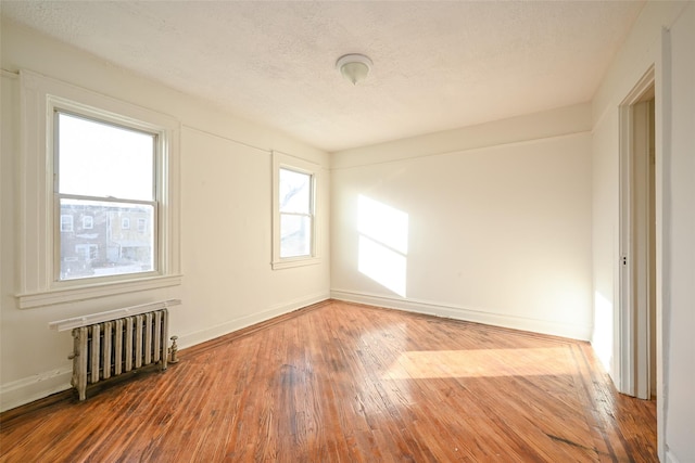 empty room with radiator heating unit, hardwood / wood-style floors, and a textured ceiling