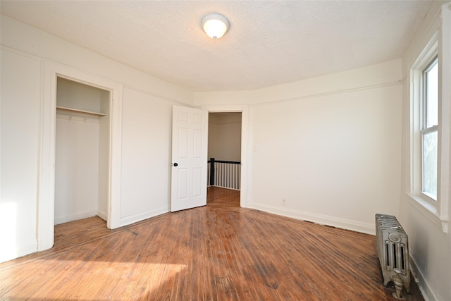 unfurnished bedroom with a closet, radiator heating unit, wood-type flooring, and a textured ceiling