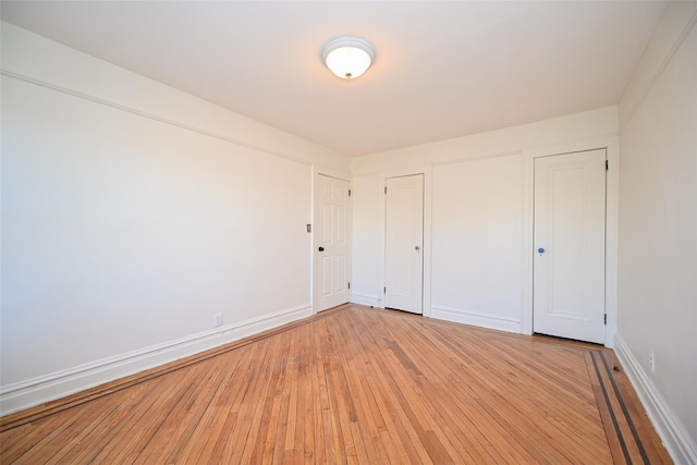 unfurnished bedroom featuring multiple closets and light hardwood / wood-style floors