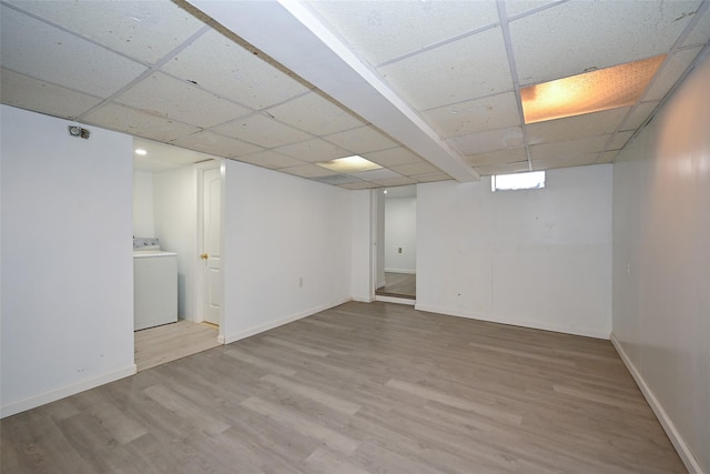 basement featuring a drop ceiling, washer / dryer, and light hardwood / wood-style flooring