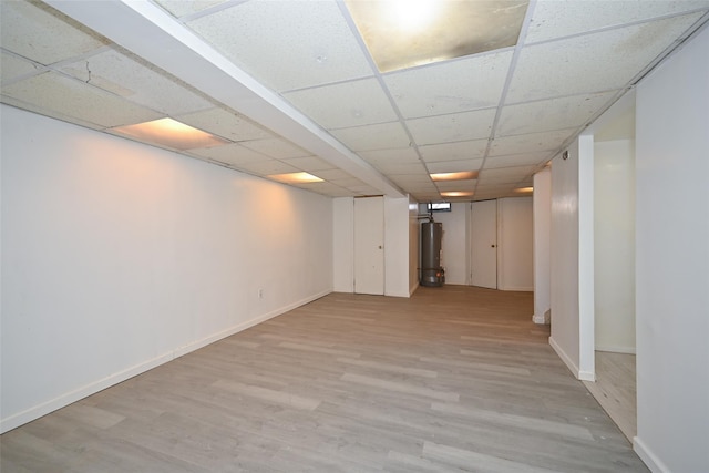 basement featuring light wood-type flooring, gas water heater, and a drop ceiling