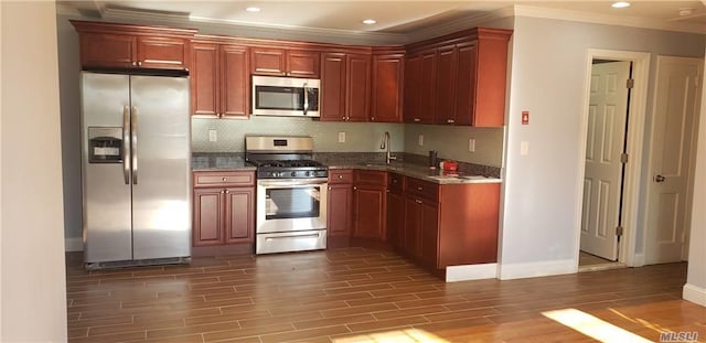 kitchen with crown molding, sink, hardwood / wood-style flooring, dark stone countertops, and appliances with stainless steel finishes