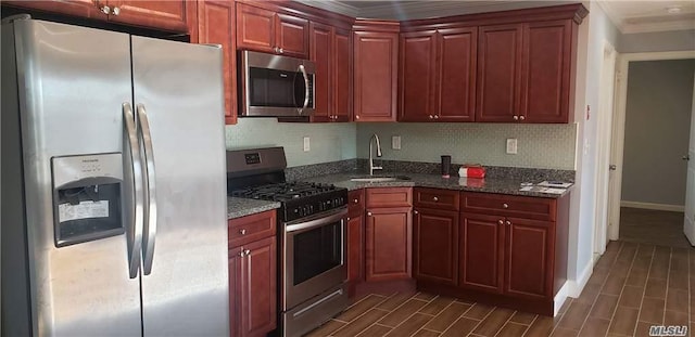 kitchen featuring appliances with stainless steel finishes, ornamental molding, dark stone countertops, and sink