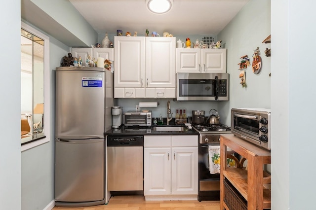 kitchen featuring a toaster, stainless steel appliances, a sink, white cabinetry, and dark countertops