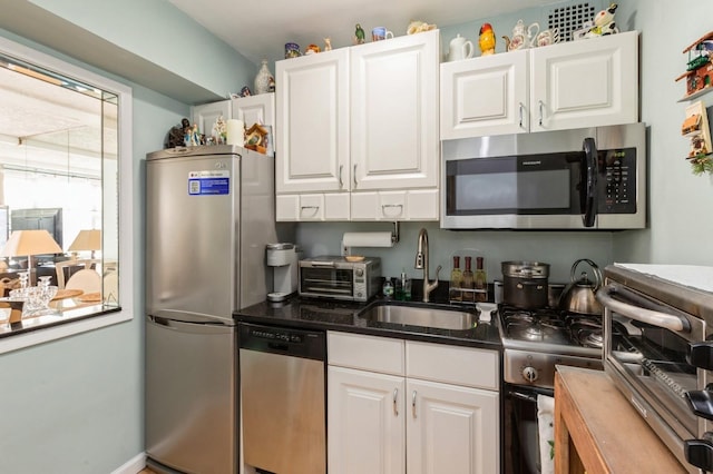 kitchen featuring dark stone counters, appliances with stainless steel finishes, a sink, and white cabinets