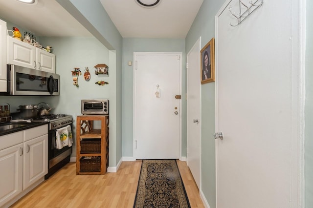 kitchen with a toaster, stainless steel appliances, dark countertops, light wood-style flooring, and white cabinets