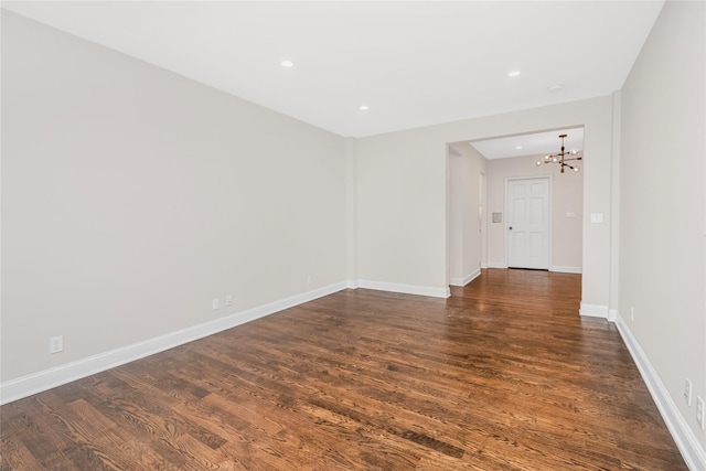 empty room with dark wood-type flooring and an inviting chandelier