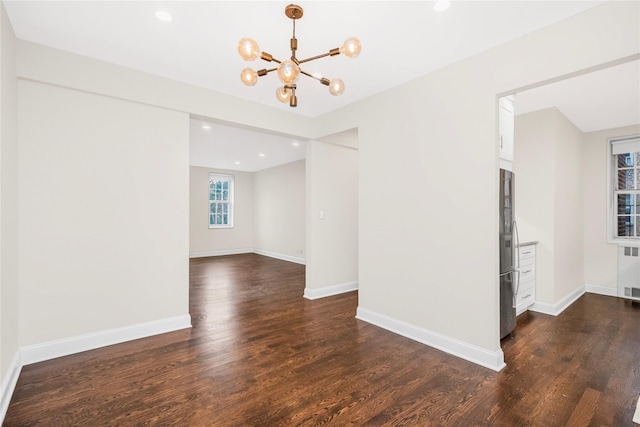 empty room featuring dark wood-type flooring, an inviting chandelier, and radiator