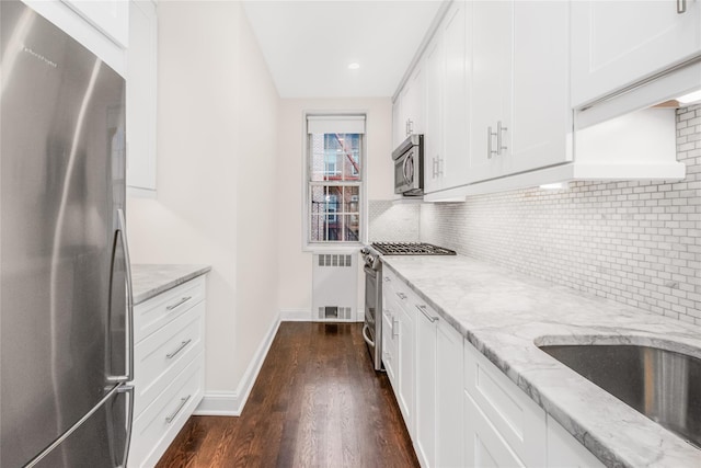 kitchen featuring appliances with stainless steel finishes, light stone countertops, dark hardwood / wood-style floors, white cabinets, and backsplash