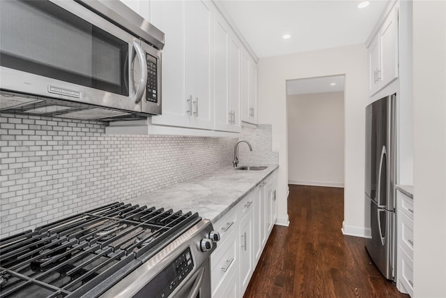 kitchen featuring light stone counters, stainless steel appliances, decorative backsplash, white cabinetry, and sink