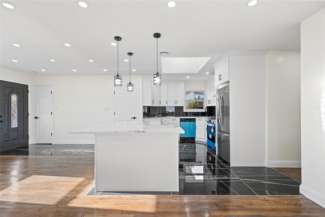 kitchen featuring appliances with stainless steel finishes, a kitchen island, white cabinetry, and decorative light fixtures