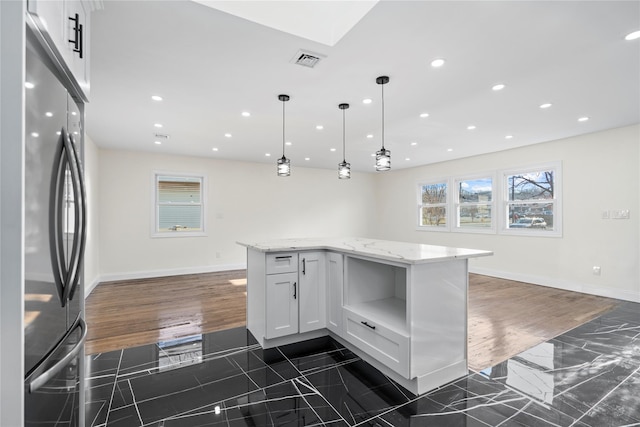 kitchen featuring decorative light fixtures, light stone countertops, white cabinetry, and stainless steel refrigerator