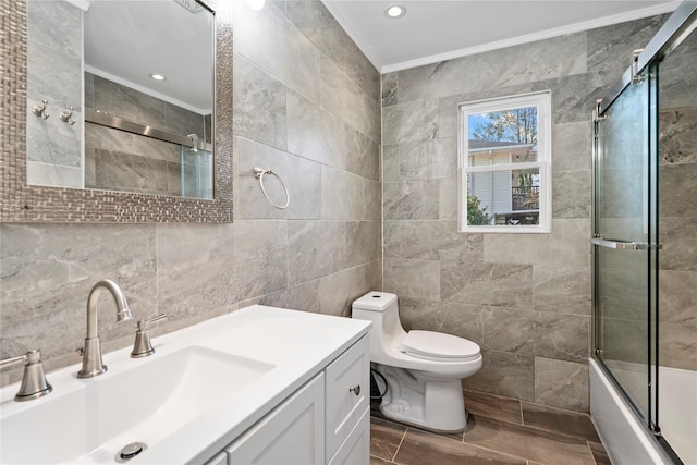 full bathroom featuring toilet, bath / shower combo with glass door, tile walls, vanity, and crown molding