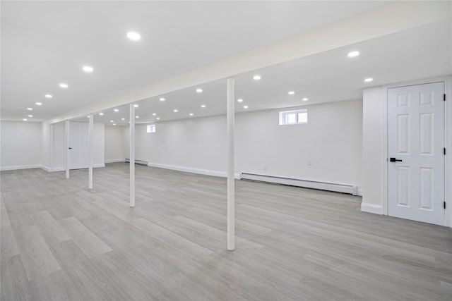 basement with a baseboard heating unit and light hardwood / wood-style flooring