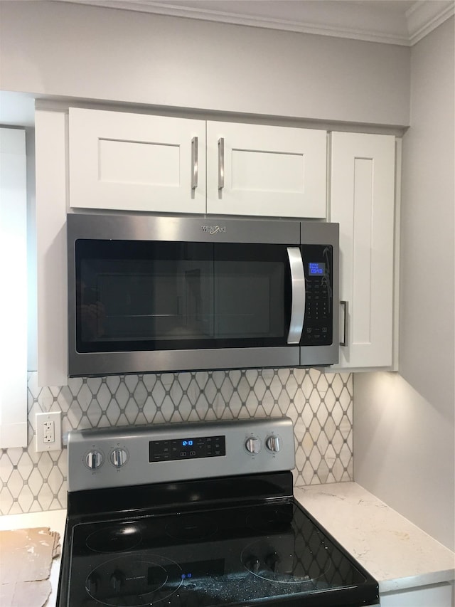 kitchen featuring white cabinets, stainless steel appliances, tasteful backsplash, light stone counters, and crown molding