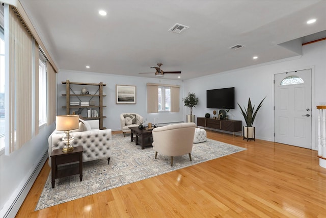 living room with baseboard heating, ornamental molding, and light wood-type flooring