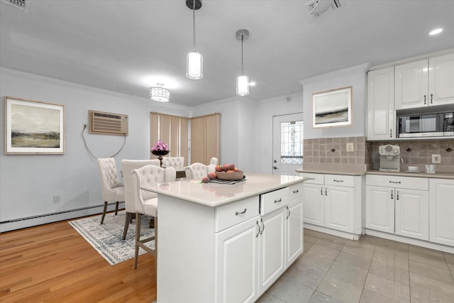 kitchen featuring a wall unit AC, built in microwave, decorative light fixtures, white cabinets, and a kitchen island