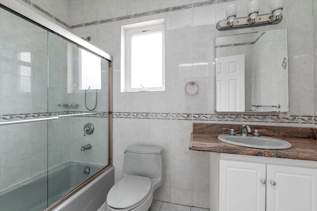 full bathroom with shower / bath combination with glass door, tile patterned flooring, vanity, tile walls, and toilet