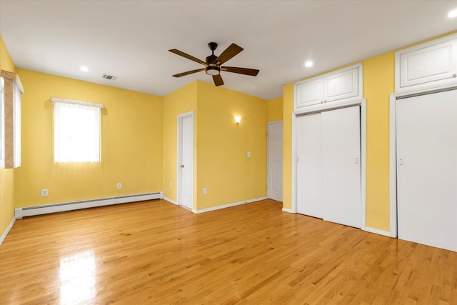 unfurnished bedroom with a baseboard radiator, light hardwood / wood-style floors, two closets, and ceiling fan