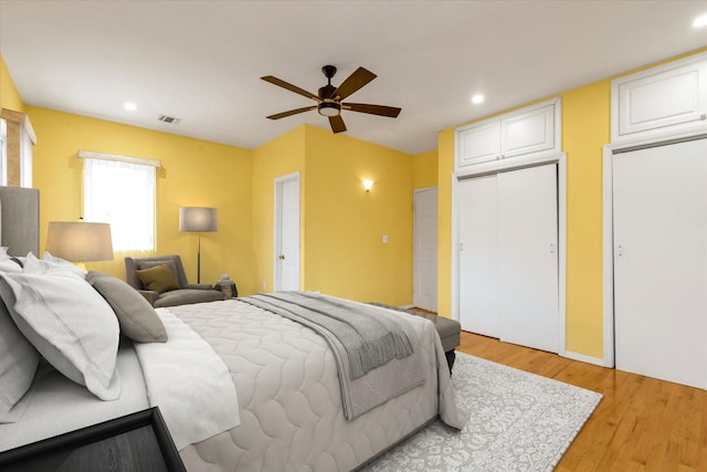 bedroom with light hardwood / wood-style floors, two closets, and ceiling fan